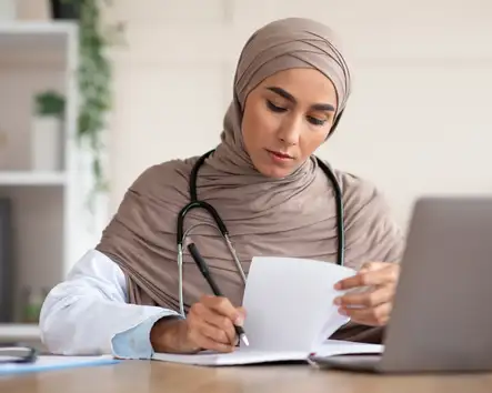 Concentrated young woman medical professional taking notes with laptop