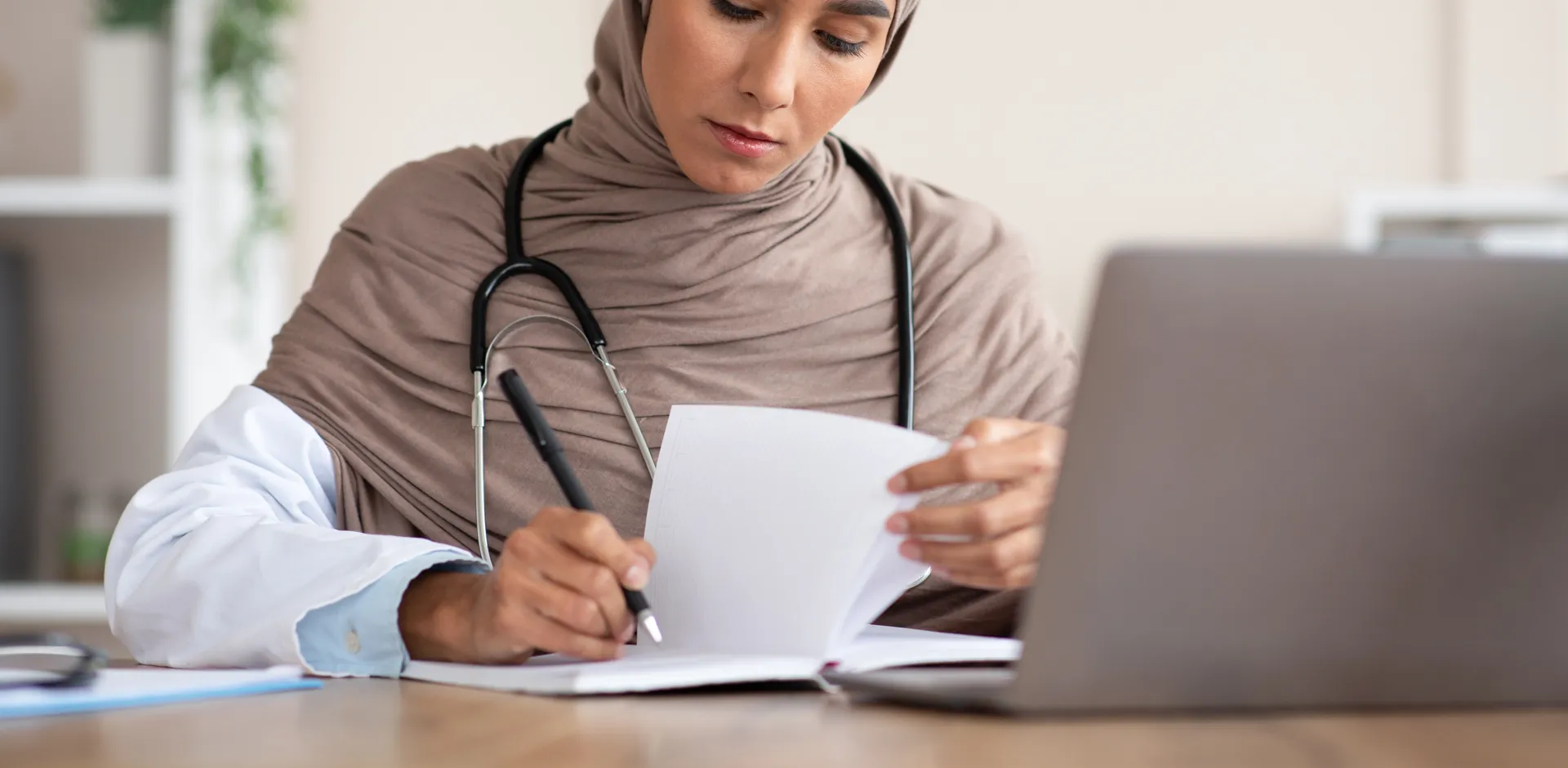 Concentrated young woman medical professional taking notes with laptop