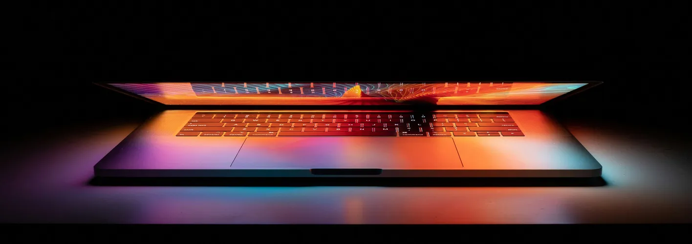Blog_Technology_partially open laptop in a dark space reflecting a colorful screen on keyboard (Web Optimized)